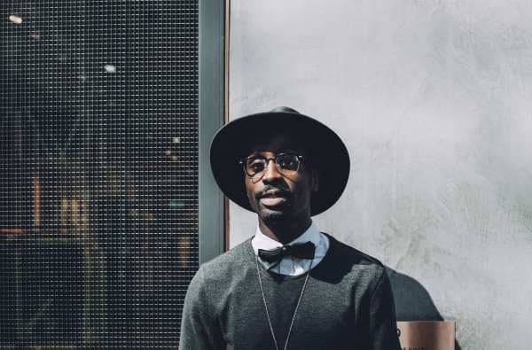 Man wearing a hat and stylish clothes in an outdoor setting.